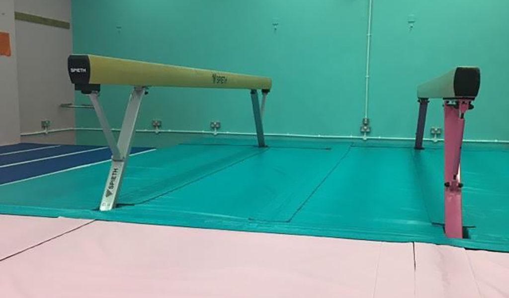 Green fitted matting beneath a gymnastics balance beam