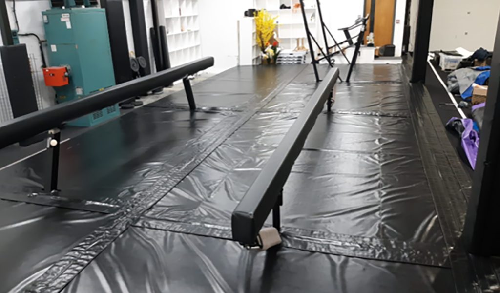 Black padded walkway beside gymnastics equipment