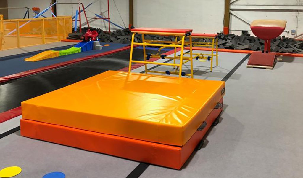 Orange and yellow landing mats beside gymnastics apparatus